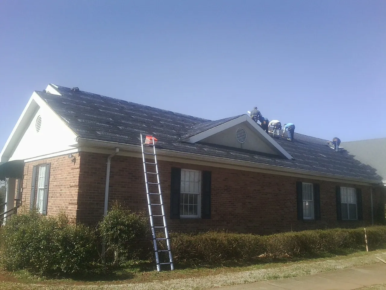 Crew tearing shingles off a brick ranch roof with a ladder set — Emergency Roof Repair work by our crew in Fountain Run