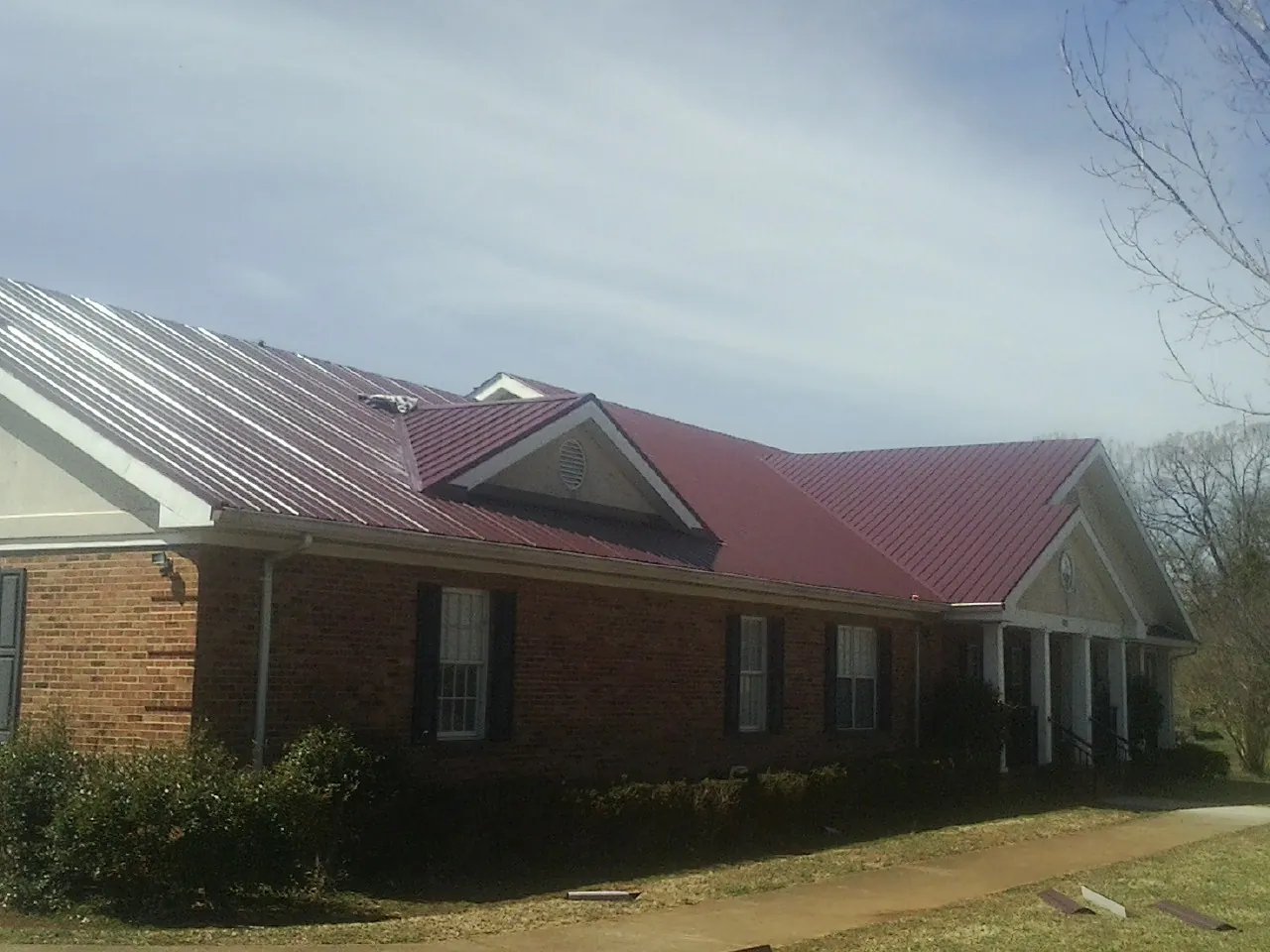 Red metal roof with gabled entries on a long brick building, from a Hail Damage Roof Repair job in Fountain Run