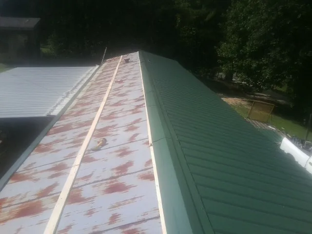 Old rusted panels beside newly installed green metal roofing — Wind Damage Roof Repair by Roofing Brothers in Fountain Run