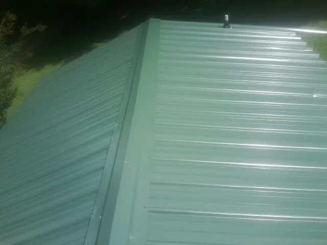 New green metal panels meeting at the ridge of a roof — Flat Roof Repair work by our crew in Fountain Run