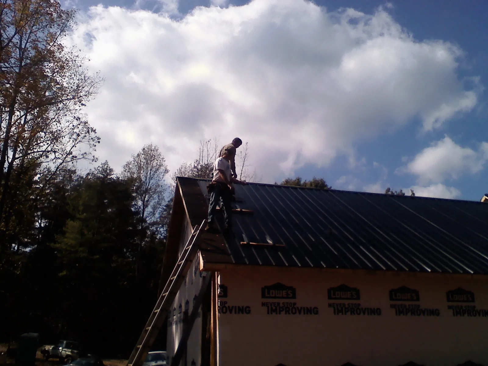 Roofer fastening dark metal panels high against a cloudy sky, from a Roof Inspection job in Fountain Run
