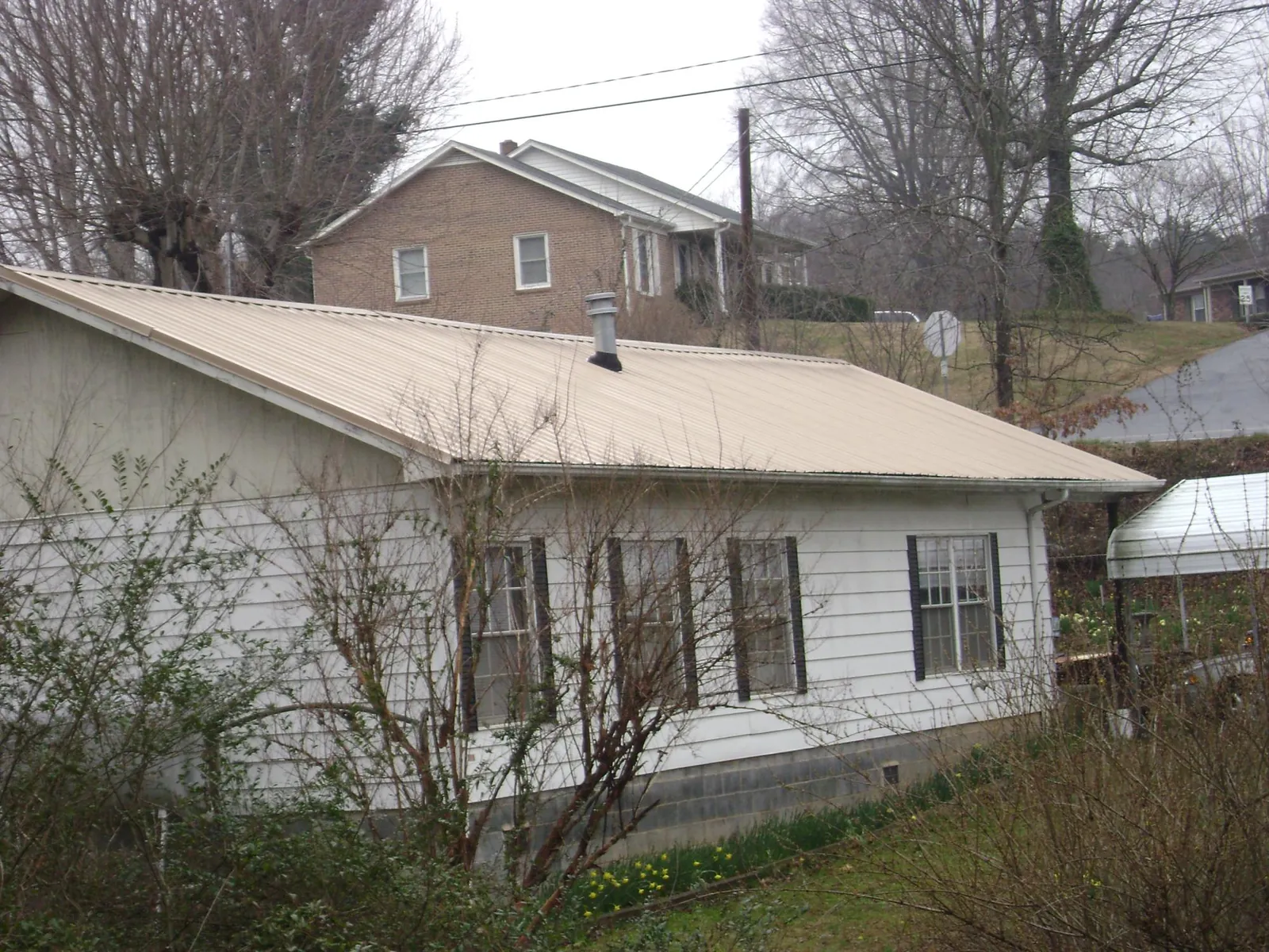 Tan metal roof on a white sided house set into a hillside — Commercial Roofing by Roofing Brothers in Fountain Run